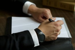 a-person-in-a-suit-writing-on-a-document-.jpg A person in a suit writing on a document.